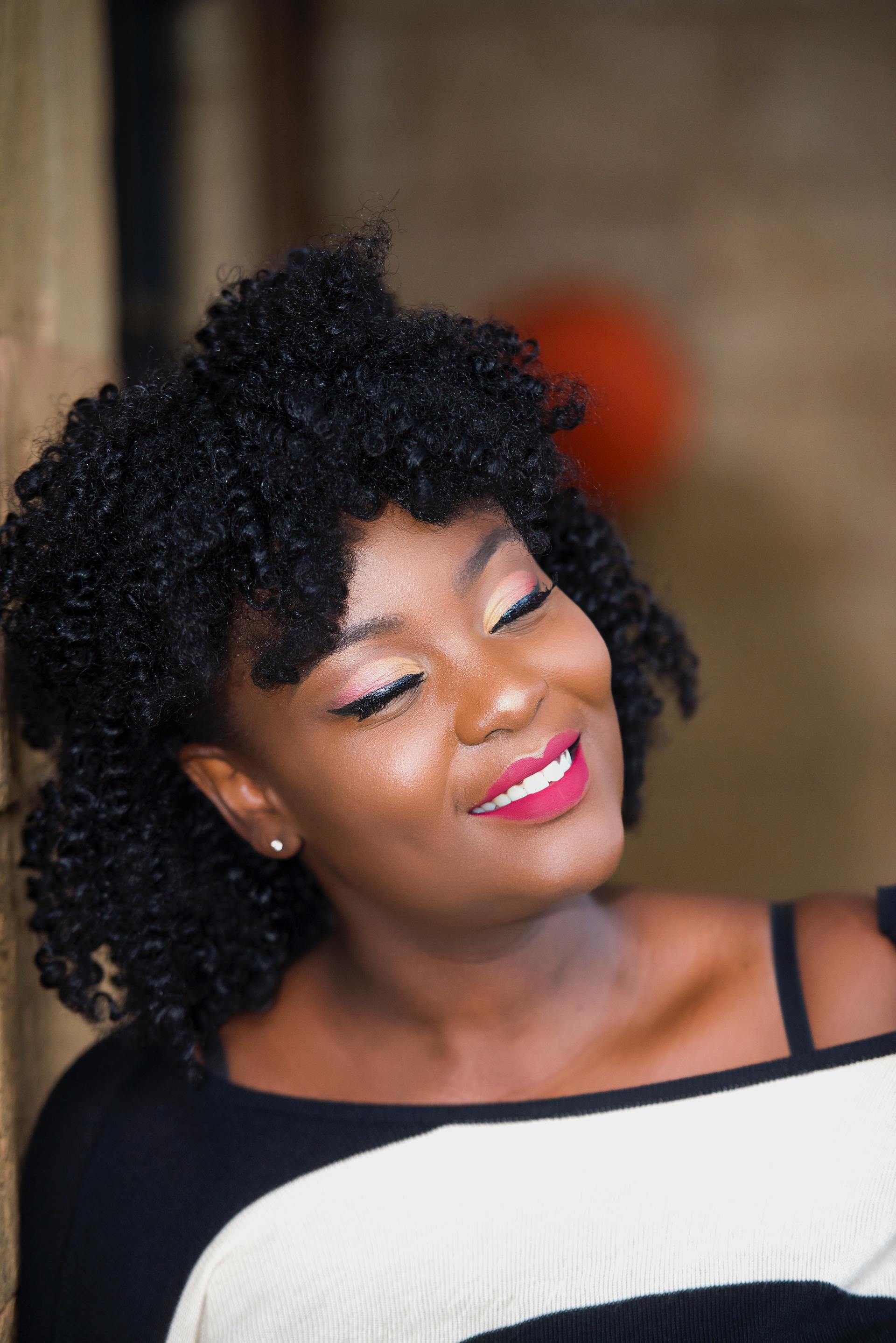 A woman with curly hair and red lipstick is smiling.